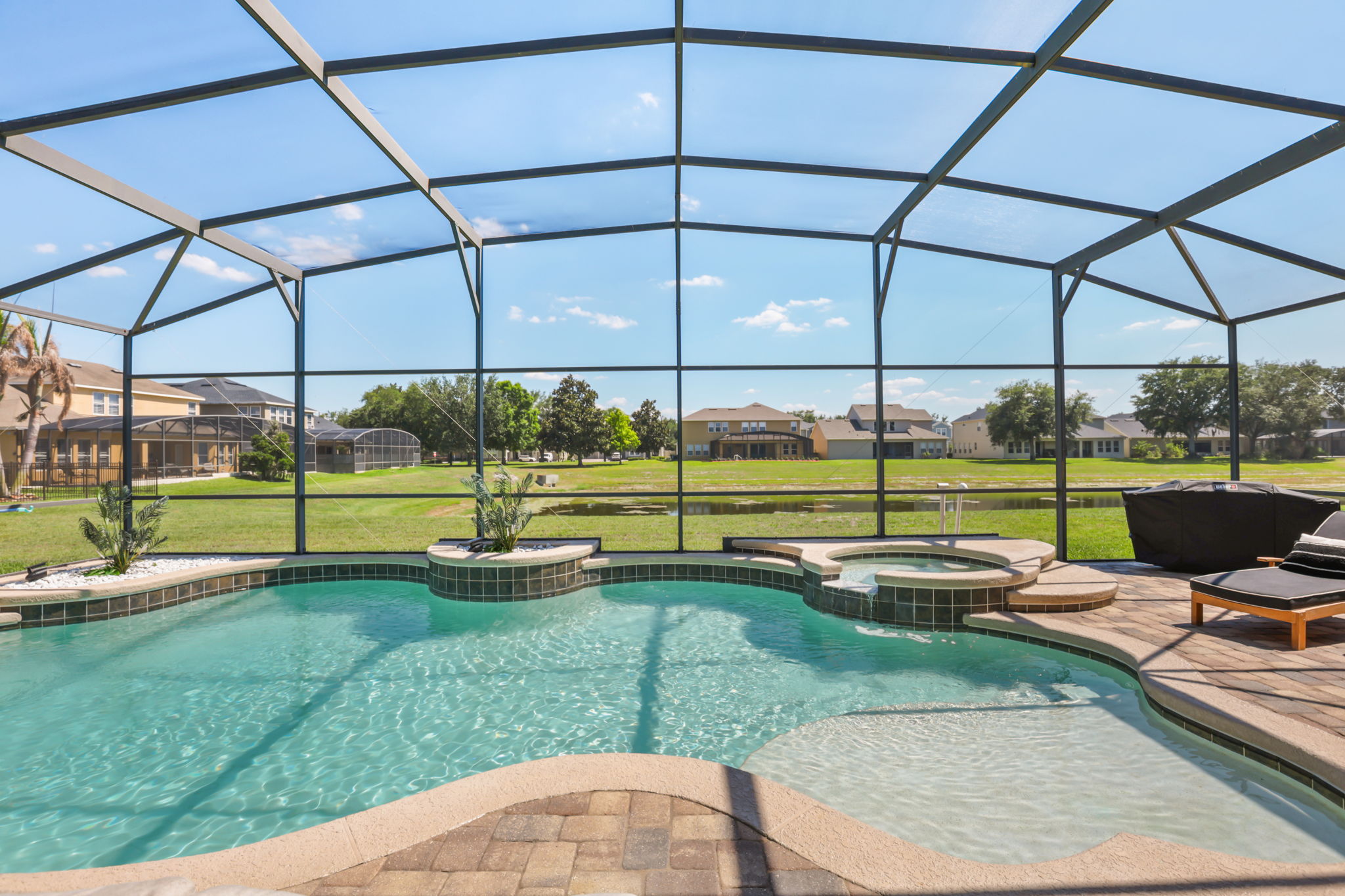 Heated pool and in-ground spa with open water views behind the screened enclosure